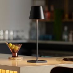 a table lamp sitting on top of a white counter next to a bowl of fruit