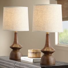 two lamps sitting on top of a wooden table next to a book and lamp shade