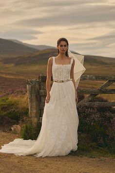 a woman in a wedding dress standing by a fence