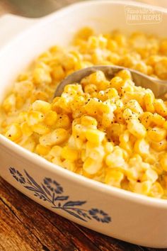 a white bowl filled with corn on top of a wooden table next to a spoon