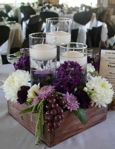 a wooden box filled with purple and white flowers next to candles on top of a table