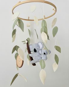 a stuffed koala bear hanging from a tree branch with leaves and branches around it