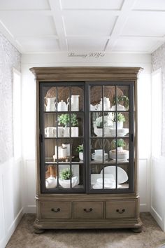 an old china cabinet with glass doors and white dishes on it's shelves in the corner