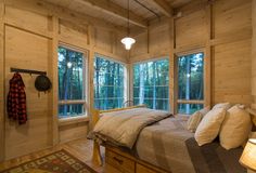 a bedroom with wooden walls and flooring has windows that look out onto the woods