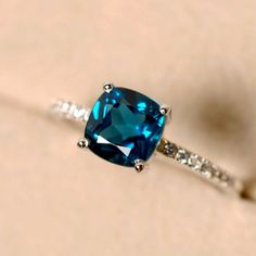 a blue diamond ring sitting on top of a white surface with diamonds around it's edges