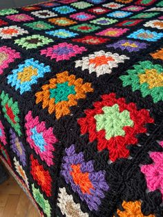 a multicolored crocheted granny blanket on top of a wooden bed frame