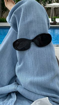 a person with sunglasses covering their face sitting by a swimming pool wearing a blue towel