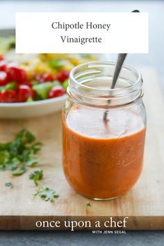 a glass jar filled with sauce sitting on top of a cutting board next to a bowl of vegetables