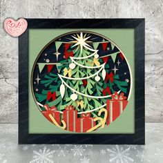 a christmas tree with presents under it in a black frame on a white wall next to snowflakes