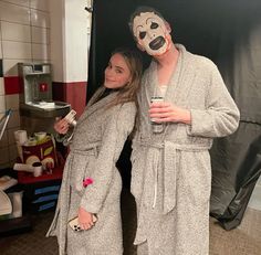 two women standing next to each other in a bathroom with masks on their faces and one holding a cup