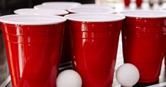 red cups with white lids are lined up on a counter next to two eggs in front of them