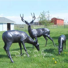 three metal deer statues in the grass near a barn