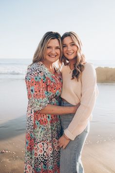 two women standing next to each other on the beach with their arms around each other