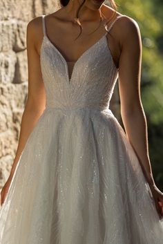 a woman wearing a wedding dress standing in front of a stone wall