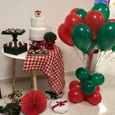 a table topped with lots of red and green balloons next to a cake covered in white frosting