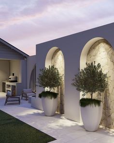 an outdoor living area with potted plants and stone arches on the side of a house