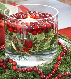 a glass bowl filled with berries and greenery on top of a red table cloth