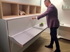 a man standing next to a white cabinet with plants in it and another person reaching for the drawer