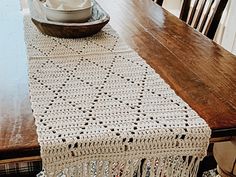 a crocheted table runner sits on top of a wooden dining room table in front of a bowl of flowers