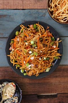 two bowls filled with noodles and carrots on top of a wooden table next to other dishes