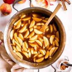 apples are being cooked in a pot with spoons and cinnamon sticks on the side