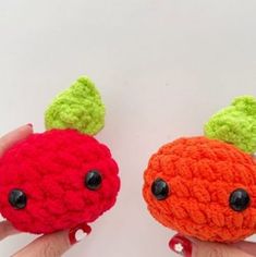 two small crocheted fruits are being held by someone's hand on a white surface