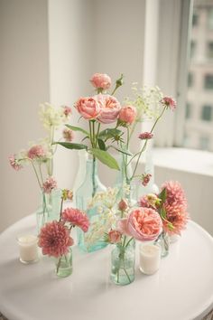 an image of flowers in glass vases on a white table with candles and windows