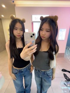 two young women taking a selfie in front of a mirror with their cell phones