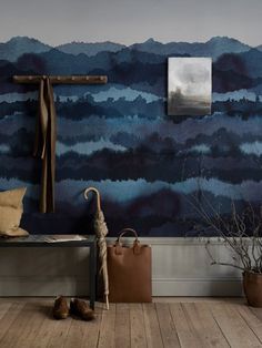 a wooden bench sitting in front of a wall covered in blue watercolors with a cross hanging on it