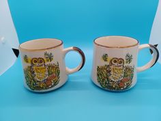 two coffee mugs sitting next to each other on a blue tablecloth covered surface