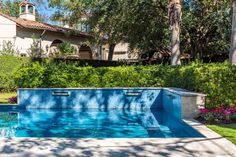 an outdoor swimming pool in front of a house with trees and bushes around it, surrounded by greenery