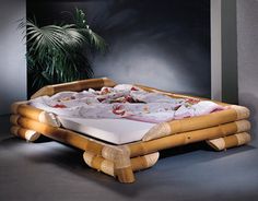 a bed made out of bamboo with white sheets and pillows on the bottom, sitting in front of a potted plant