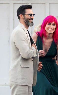 a man in a suit and pink hair standing next to a woman with bright pink hair