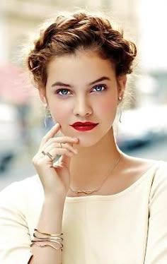 a beautiful young lady posing in front of a building with her hand on her chin