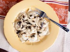 a yellow plate topped with ravioli covered in cheese and black olives next to a fork