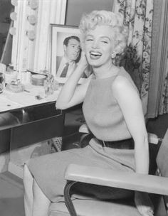 an old black and white photo of a woman sitting in front of a mirror smiling