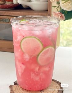 a pink drink with lime slices on the rim and ice in a glass sitting on top of a wooden slice