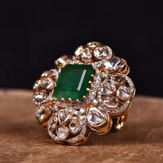 an emerald and diamond ring sitting on top of a piece of wood with diamonds around it