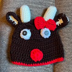 a crocheted deer hat with big eyes and a red bow on the top