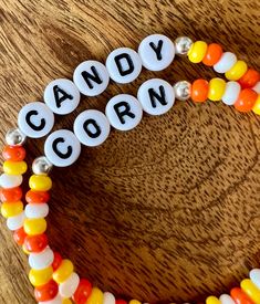 two bracelets with candy corn on them sitting on top of a wooden table next to an orange, yellow and white bead necklace