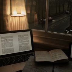 an open book sitting on top of a desk next to a laptop computer and lamp