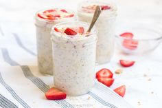 three small jars filled with yogurt and strawberries on a towel next to two spoons