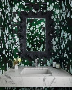 a white sink sitting under a bathroom mirror next to a green and black wallpaper