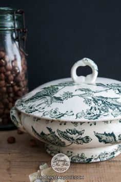 a white and green casserole dish sitting on top of a wooden table next to a jar