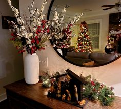 a living room decorated for christmas with decorations and trees in the background, including a large round mirror