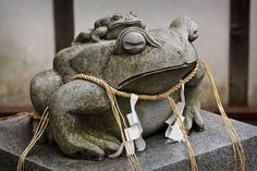 a frog statue sitting on top of a stone block with rope around it's neck