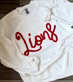 Pullover embroidered with cursive chenille Lions Team. Will be made as pictured. Please message us for custom colors, however we do have most basic colors of chenille available. *We use only the highest quality Gildan Heavy Blend Unisex Sweatshirts White Oversized Sweatshirt With School Spirit, White Varsity Sweater With Relaxed Fit, White Embroidered Logo Top For College, Long Sleeve Sweatshirt With School Spirit Embroidery, School Spirit Tops With Embroidered Text For Fall, School Spirit Embroidered Tops For Fall, Fall School Spirit Tops With Embroidered Text, College Red Tops With Embroidered Text, Red Embroidered Text College Tops