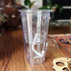 a plastic cup sitting on top of a wooden table next to a pair of scissors