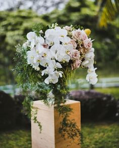 a vase filled with white and pink flowers sitting on top of a wooden block in the grass