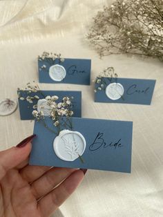 three blue cards with white flowers and the word bride written on them are being held by someone's hand